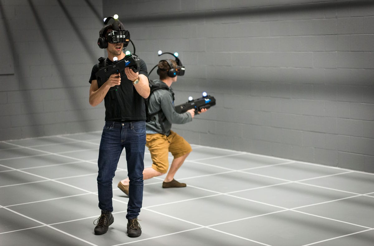 Two men walk with VR headsets and fake guns